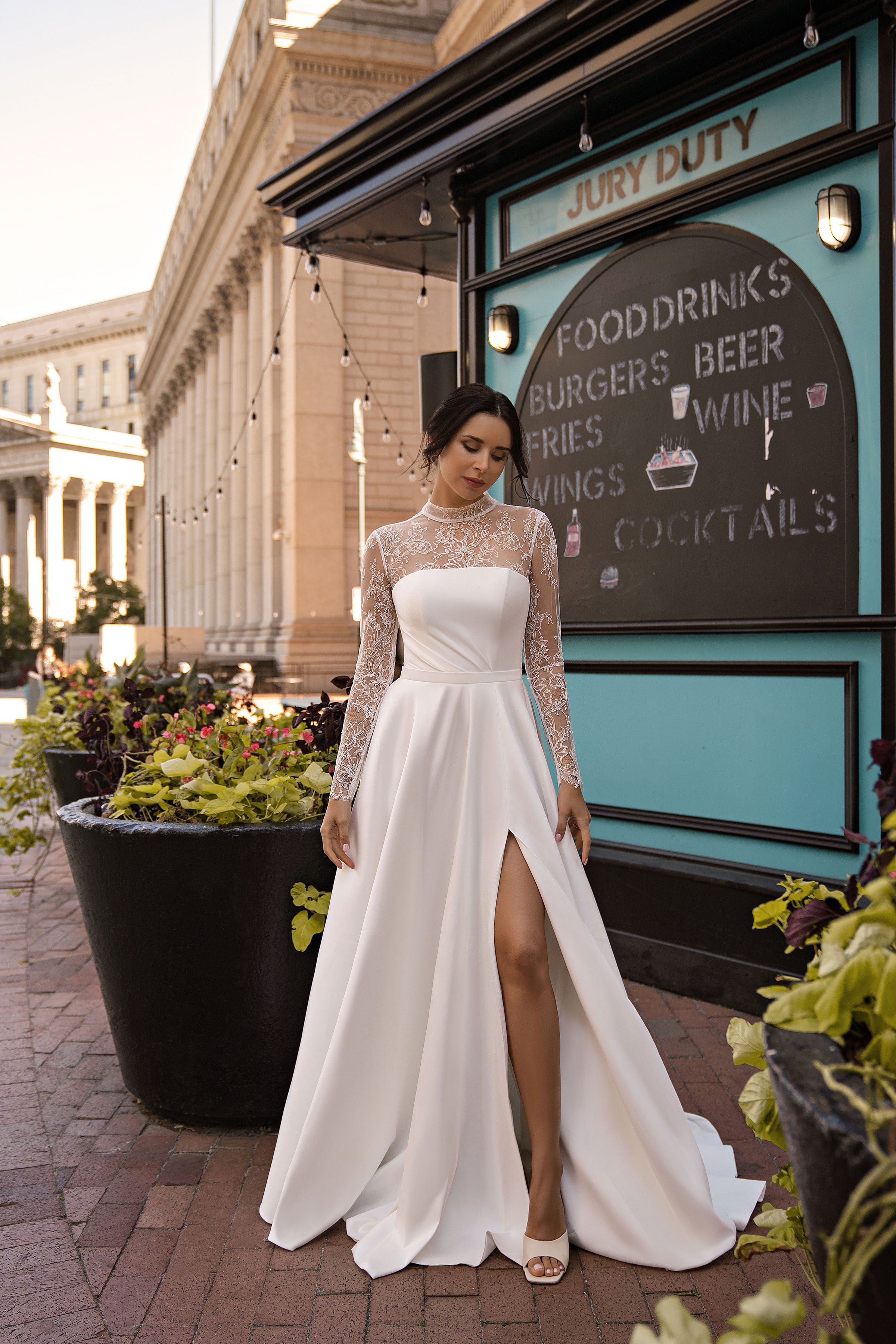 White wedding dress with sheer lace sleeves, a fitted bodice, flowing A-line skirt, and thigh-high slit