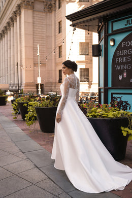 Side profile of a white A-line wedding dress with long lace sleeves and a sweeping floor-length train