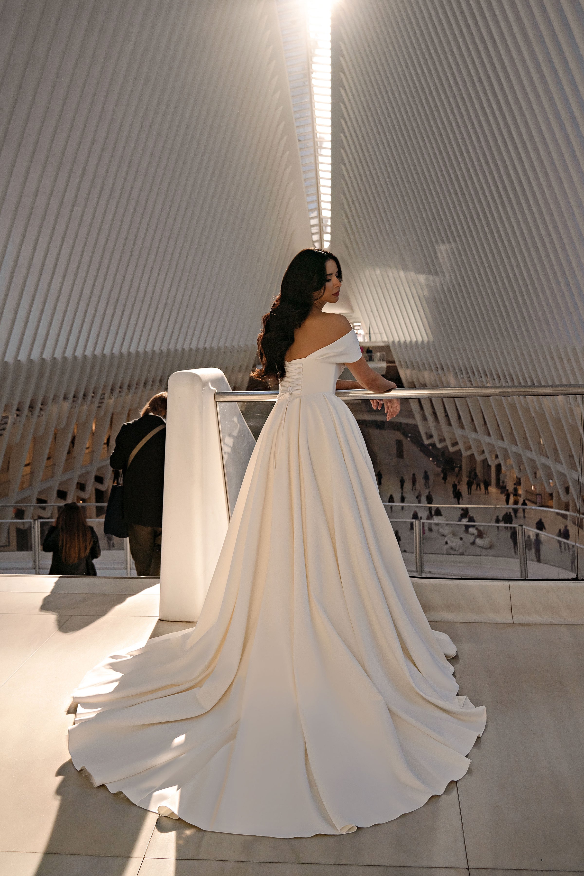 Ivory wedding dress shown from the back with an off-the-shoulder neckline and a sweeping, pleated train