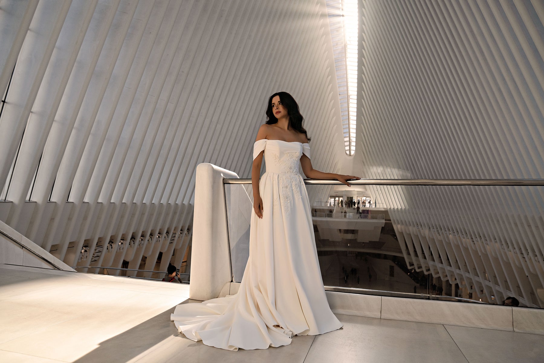 Full-length ivory wedding dress with an off-the-shoulder neckline, fitted embellished bodice, and flowing train