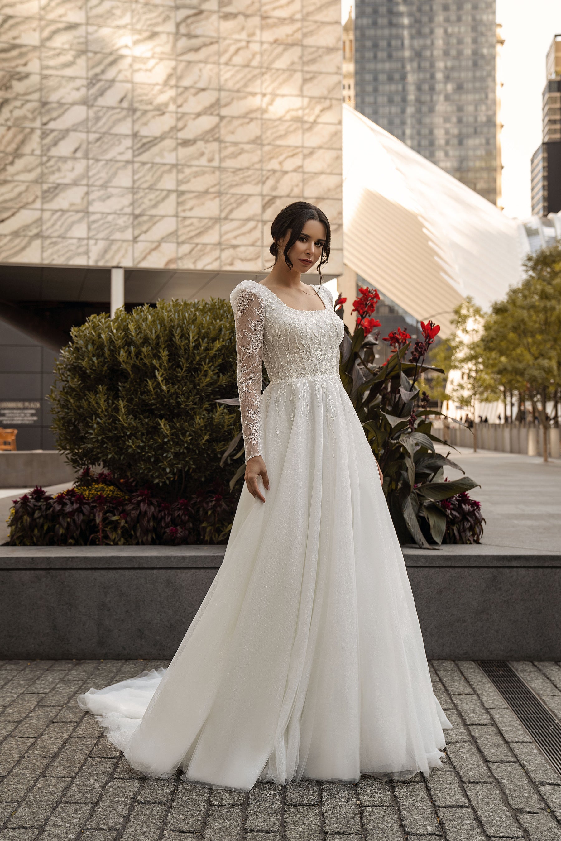 Full-length ivory A-line wedding dress with long lace sleeves, a rounded neckline, sparkling bodice, and sweeping train
