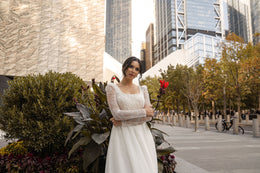 Sparkling ivory wedding dress with long floral lace sleeves, a rounded neckline, fitted bodice, and softly gathered skirt