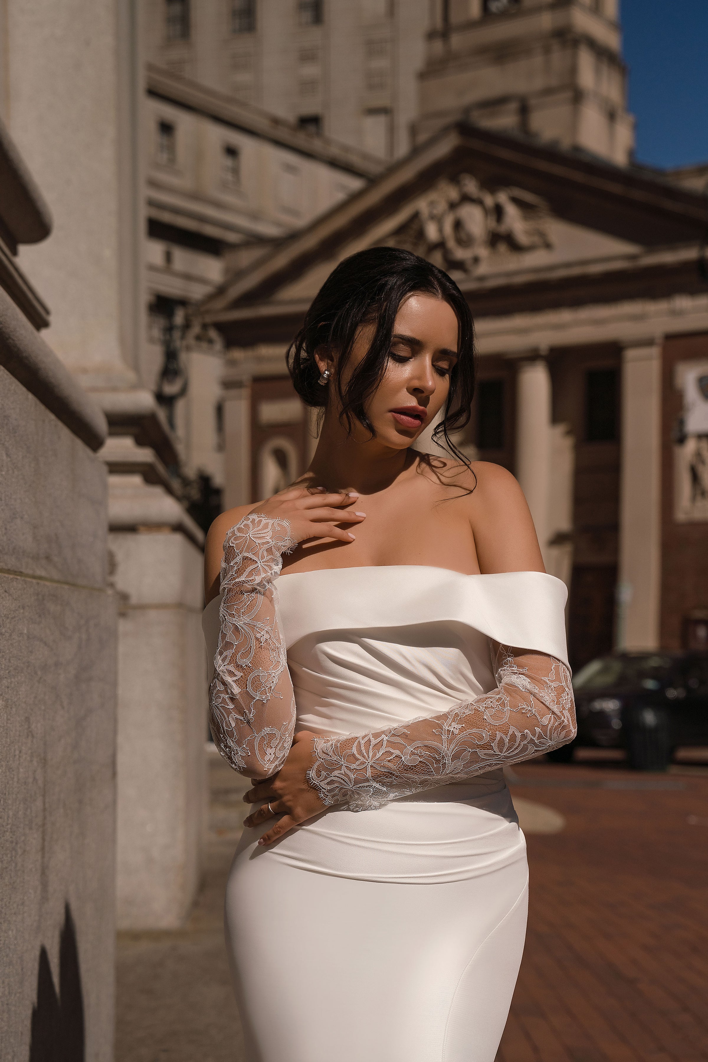 Close-up of an ivory wedding dress bodice with an off-the-shoulder neckline, ruched fabric, and sheer lace sleeves