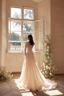 Ivory wedding dress with a beaded illusion back, long sleeves, and a flowing floor-length train