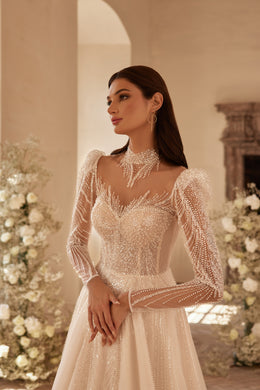 Close-up of a wedding dress bodice with dense beadwork, an illusion high neckline, and long sheer sleeves