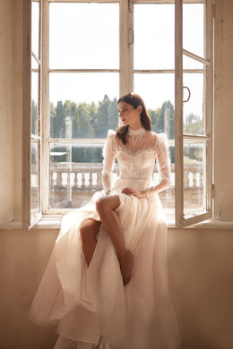 Ivory wedding dress with a beaded illusion neckline, long sheer sleeves, and a flowing full skirt