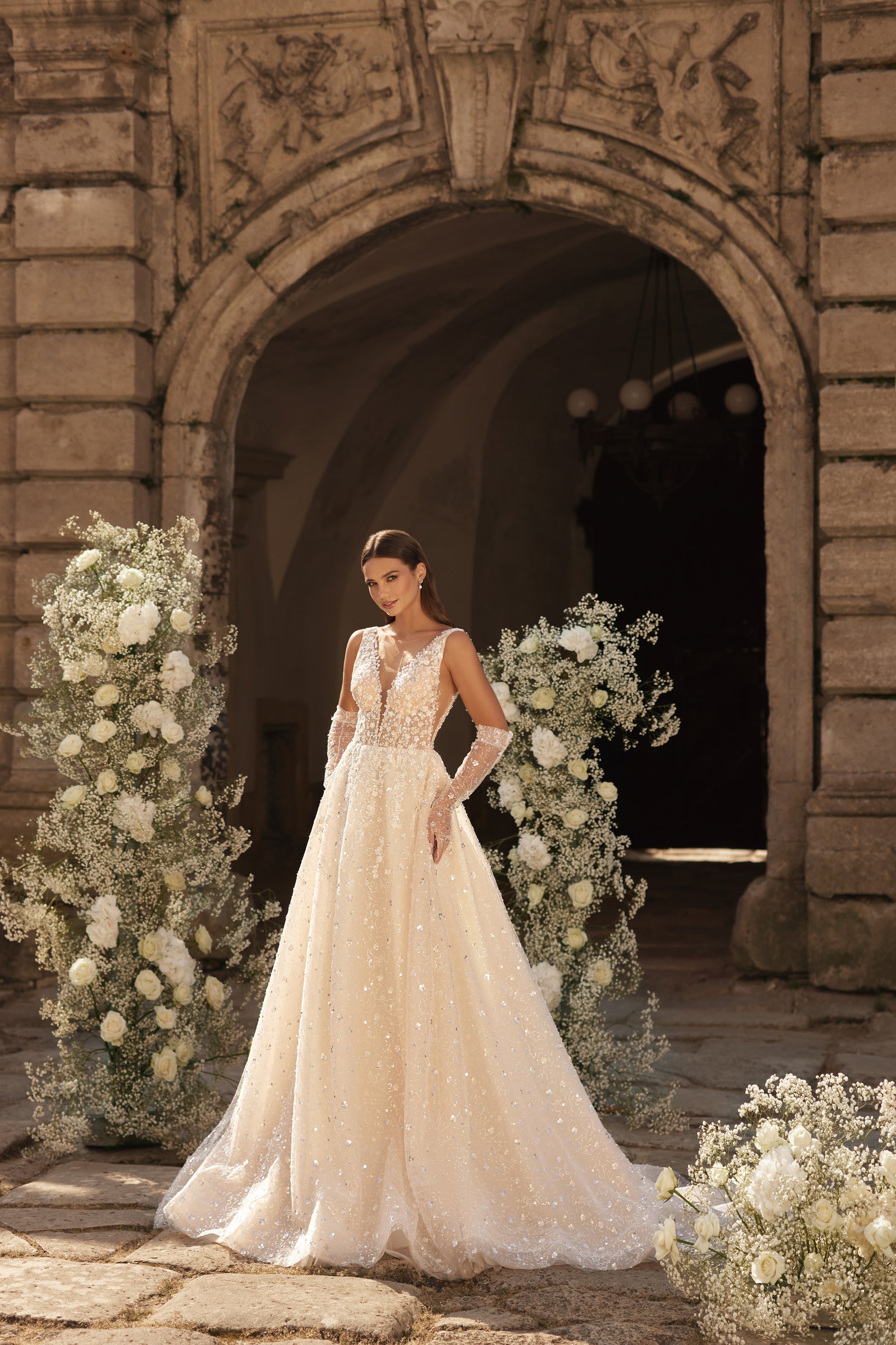 Embellished ivory wedding dress with a sheer deep V-neck, sleeveless bodice, and sweeping A-line skirt