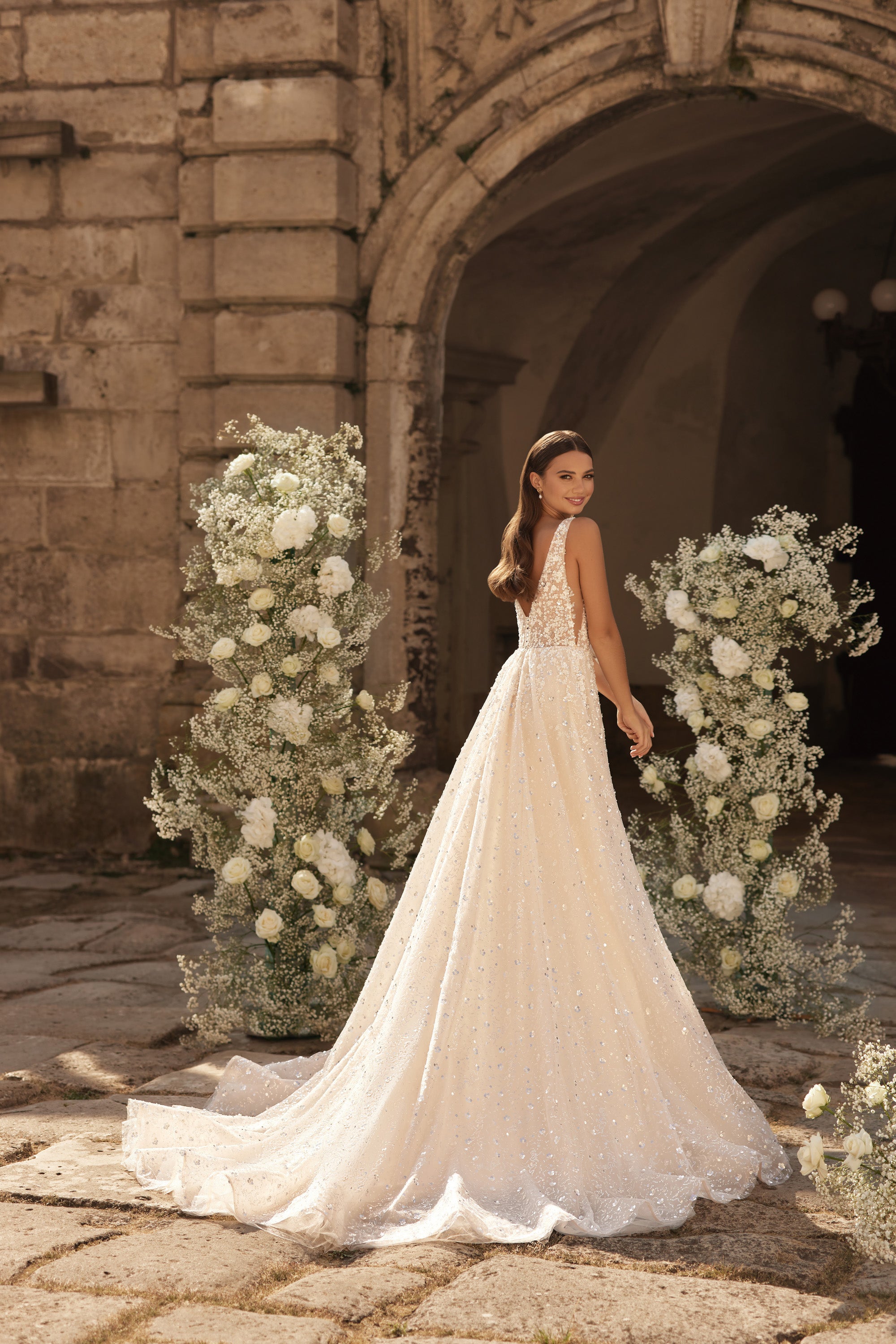 Sparkling ivory wedding dress showing its open back, flowing A-line skirt, and extended chapel train
