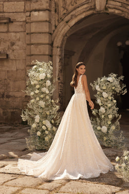 Sparkling ivory wedding dress showing its open back, flowing A-line skirt, and extended chapel train