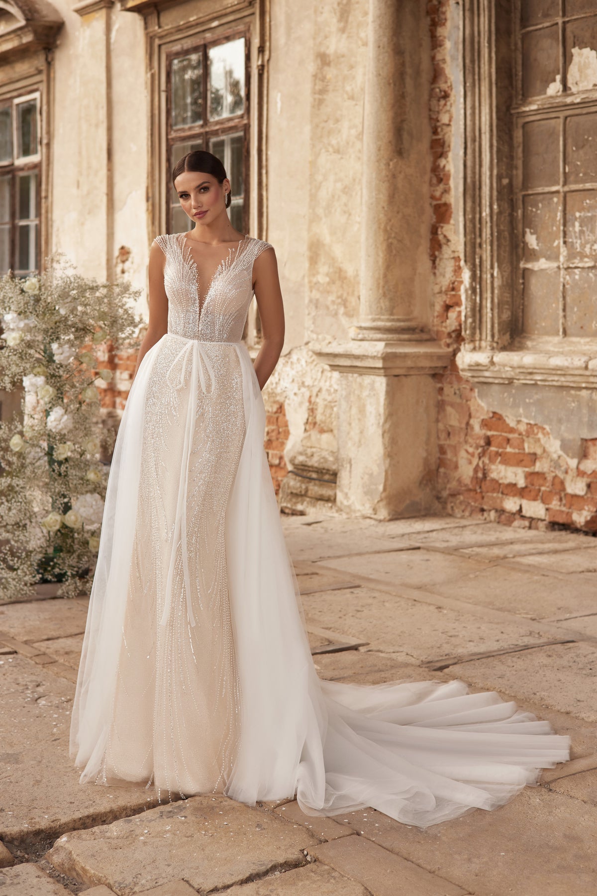 Beaded V-neck wedding dress with a sheer overskirt, fitted sheath skirt, and sweeping train