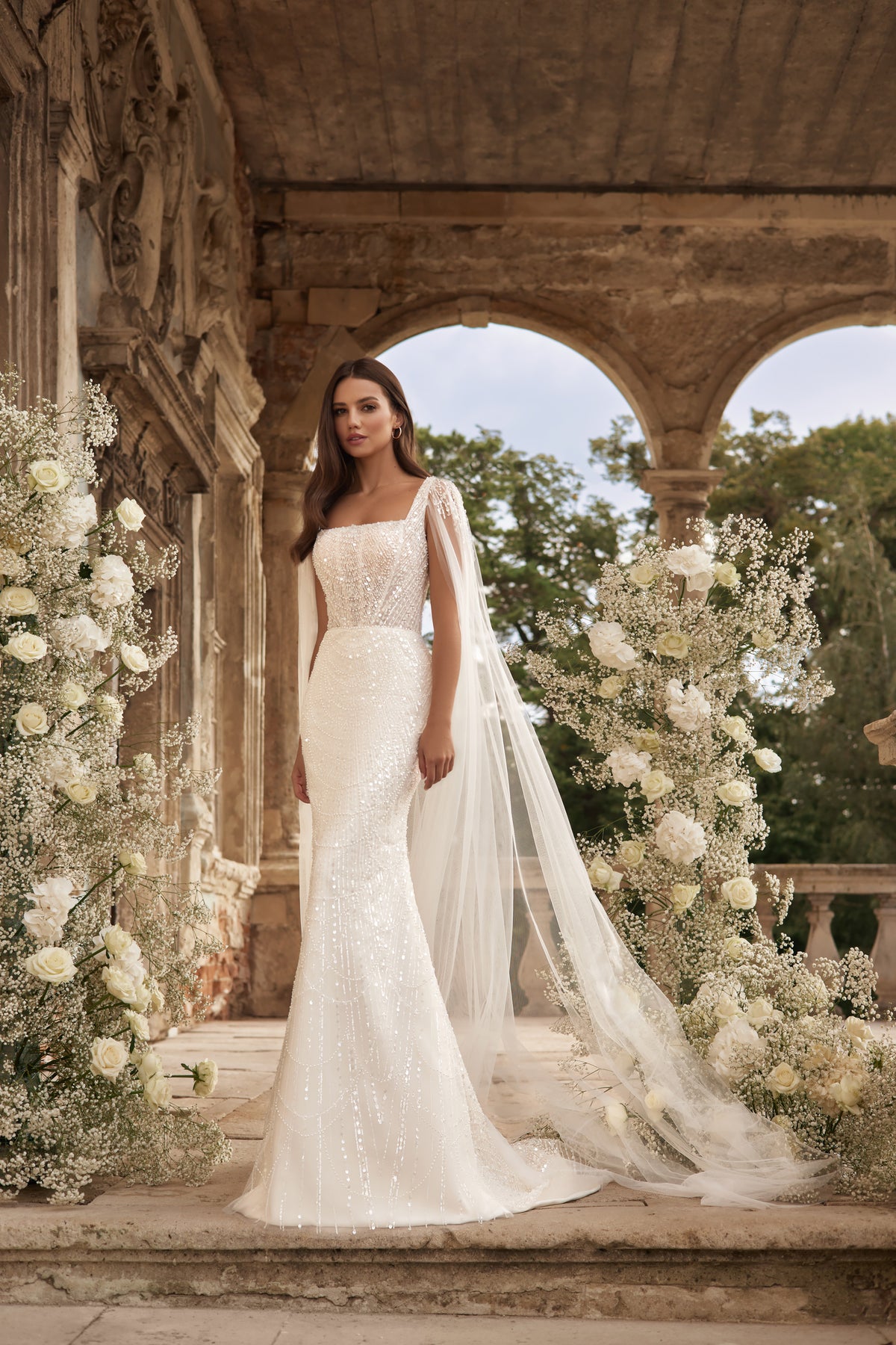 Ivory wedding dress with a square neckline, embellished bodice, sheer draped sleeves, and trailing train