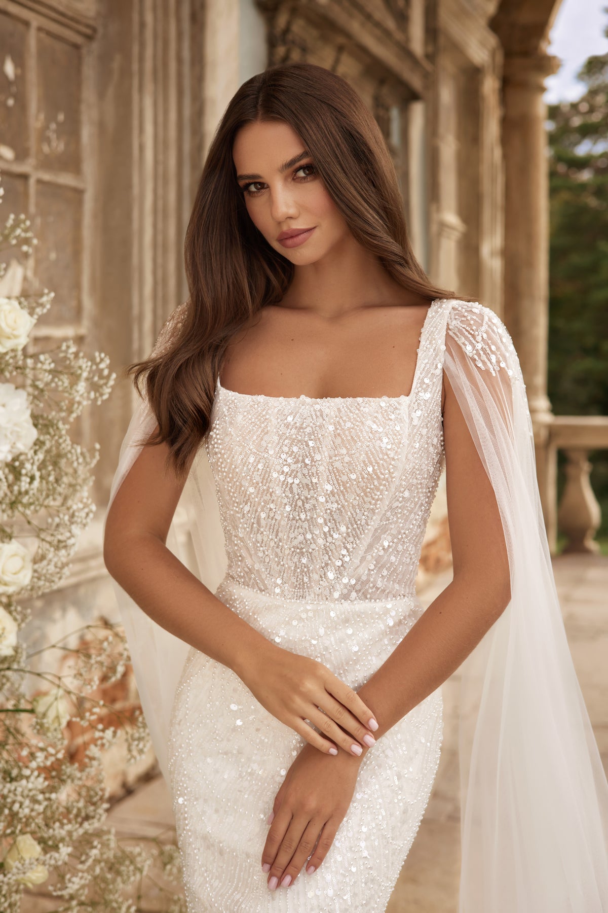 Close-up of an ivory wedding dress with a square neckline, shimmering beadwork, and sheer draped sleeves