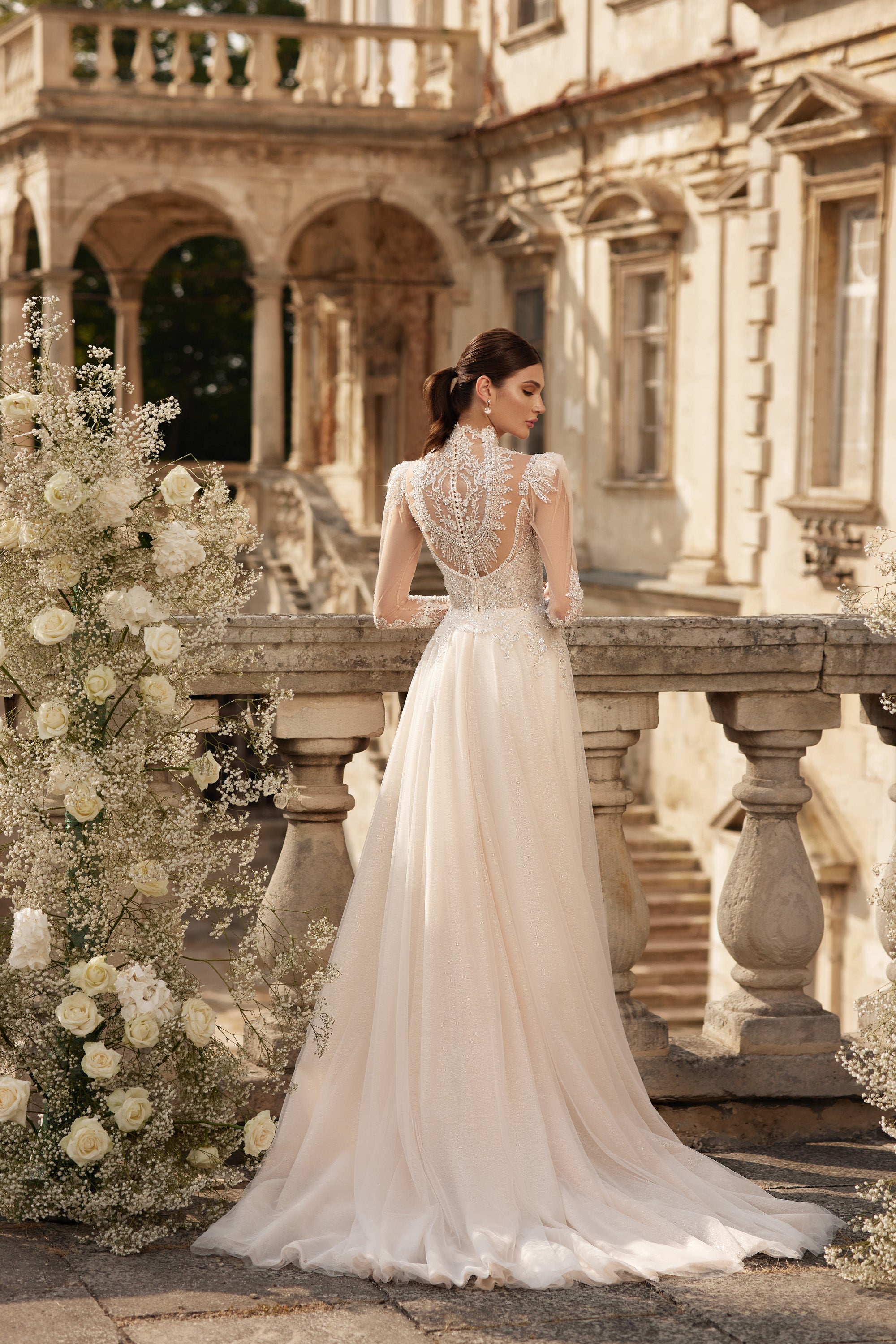 Ivory wedding dress with an ornate lace back, sheer long sleeves, fitted waist, and flowing train