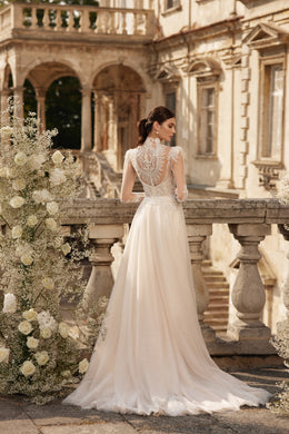 Ivory wedding dress with an ornate lace back, sheer long sleeves, fitted waist, and flowing train