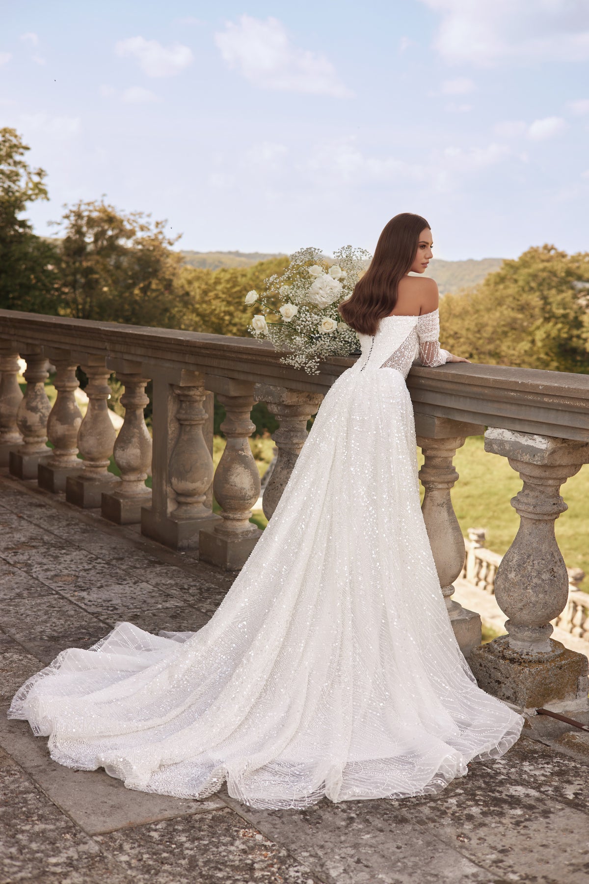 Back view of an ivory wedding dress with lace off-the-shoulder sleeves and a long, sweeping train