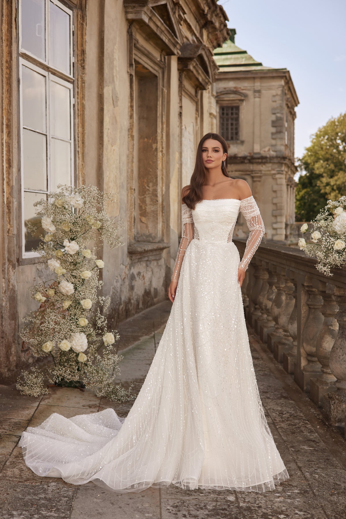 Ivory A-line wedding dress with an off-the-shoulder neckline, sheer lace sleeves, sparkle, and a train