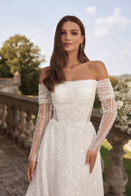 Close-up of an ivory wedding dress with a straight off-the-shoulder neckline, sheer beaded sleeves, and sparkle