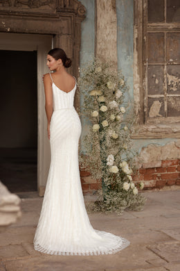 Ivory wedding dress with a low scoop back, thin straps, fitted sheath silhouette, and pooling train