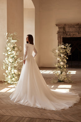 Back view of an ivory wedding dress with a sheer beaded back, long sleeves, and sweeping train
