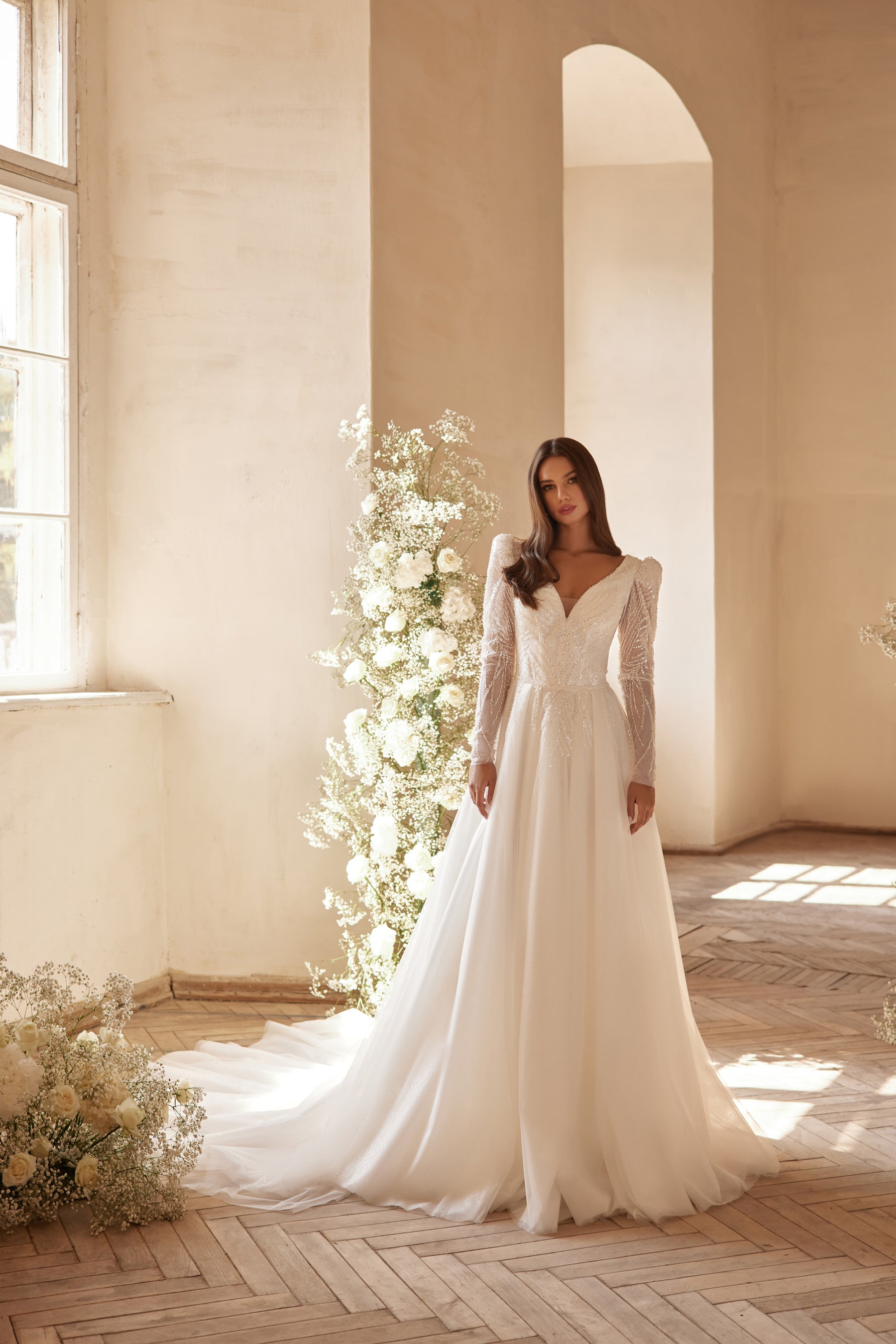 Ivory A-line wedding dress with beaded V-neckline, long sheer sleeves, and a flowing train