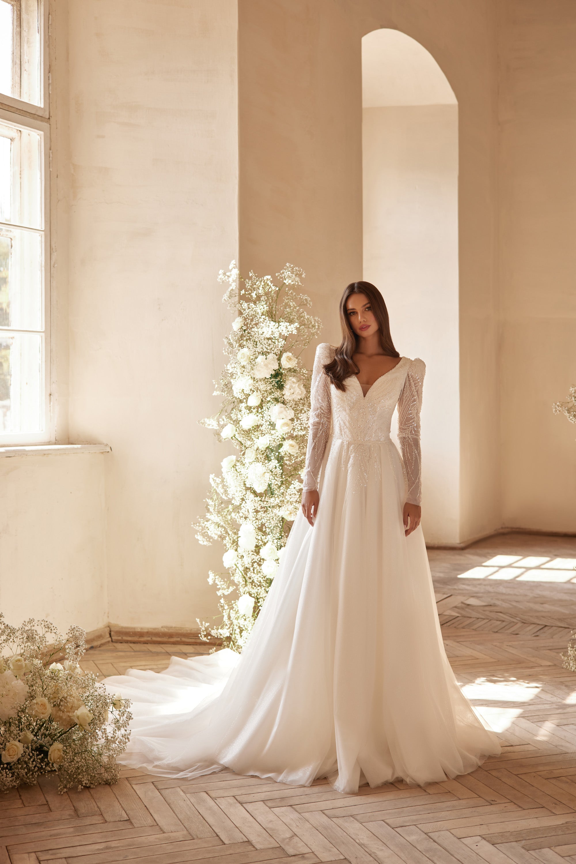 Ivory A-line wedding dress with beaded V-neckline, long sheer sleeves, and a flowing train