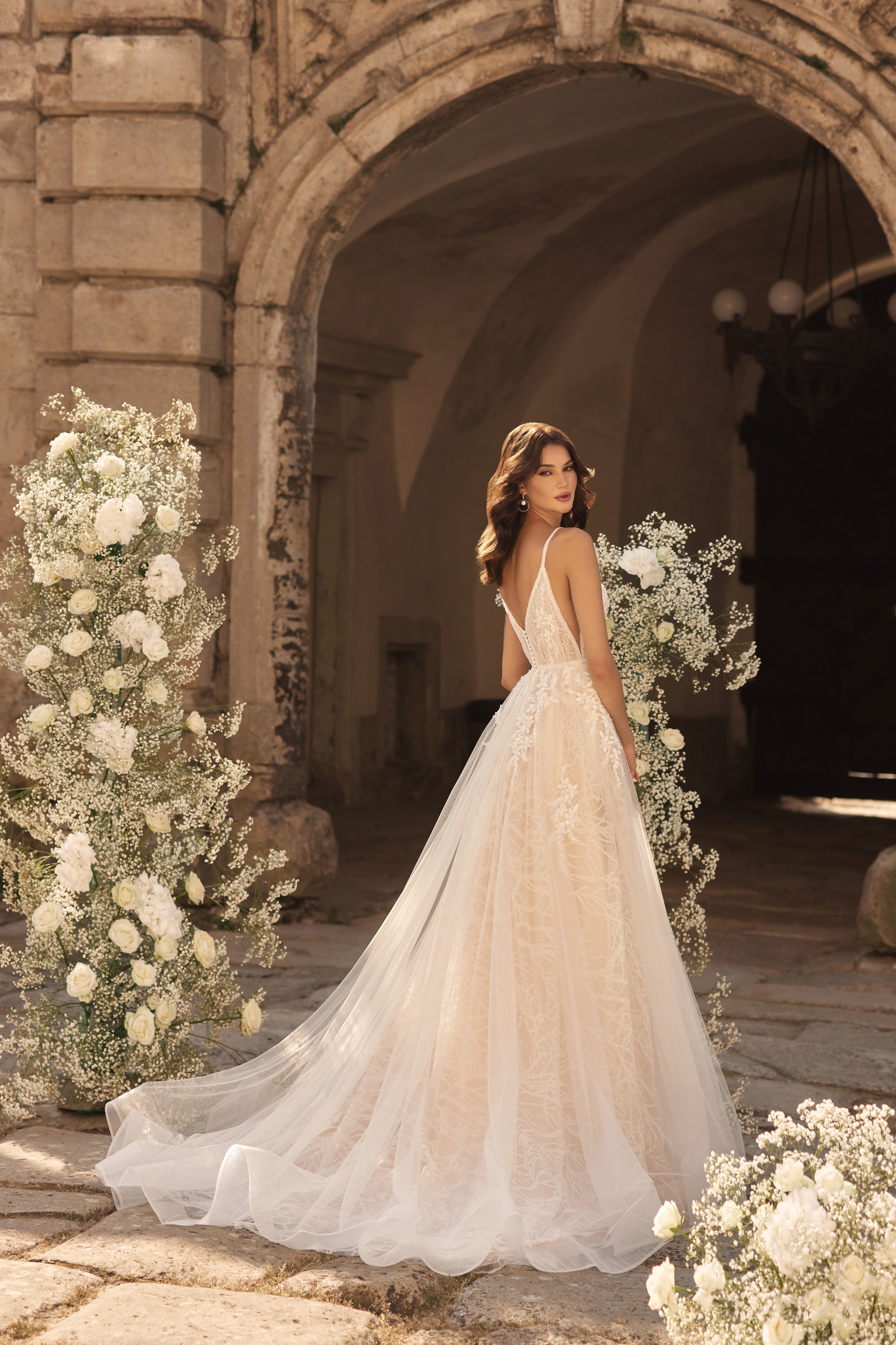Open V-back wedding dress with thin straps, floral lace, and a flowing train