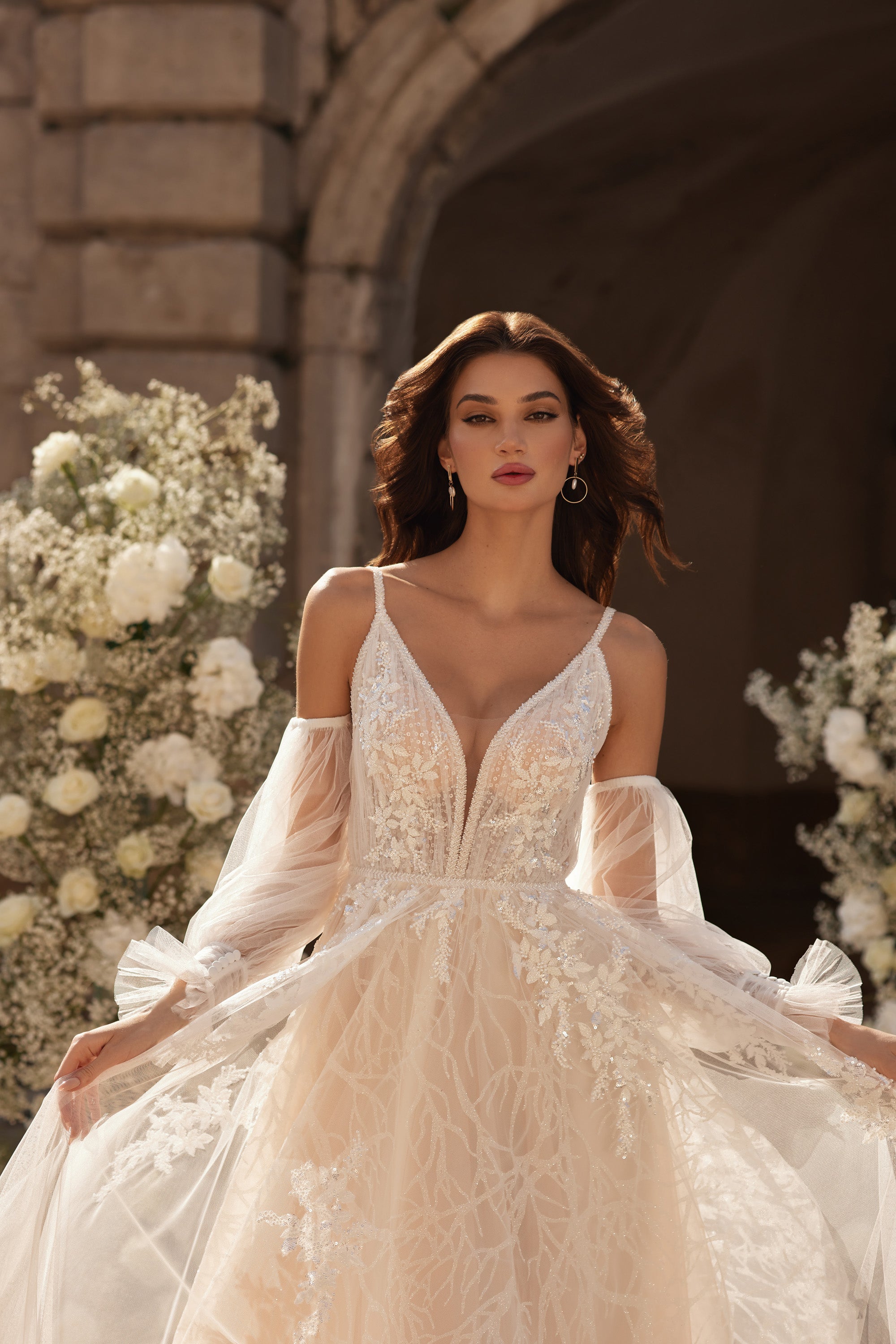 Close-up of an ivory wedding dress bodice with floral appliqués, a plunging V-neck, and sheer sleeves