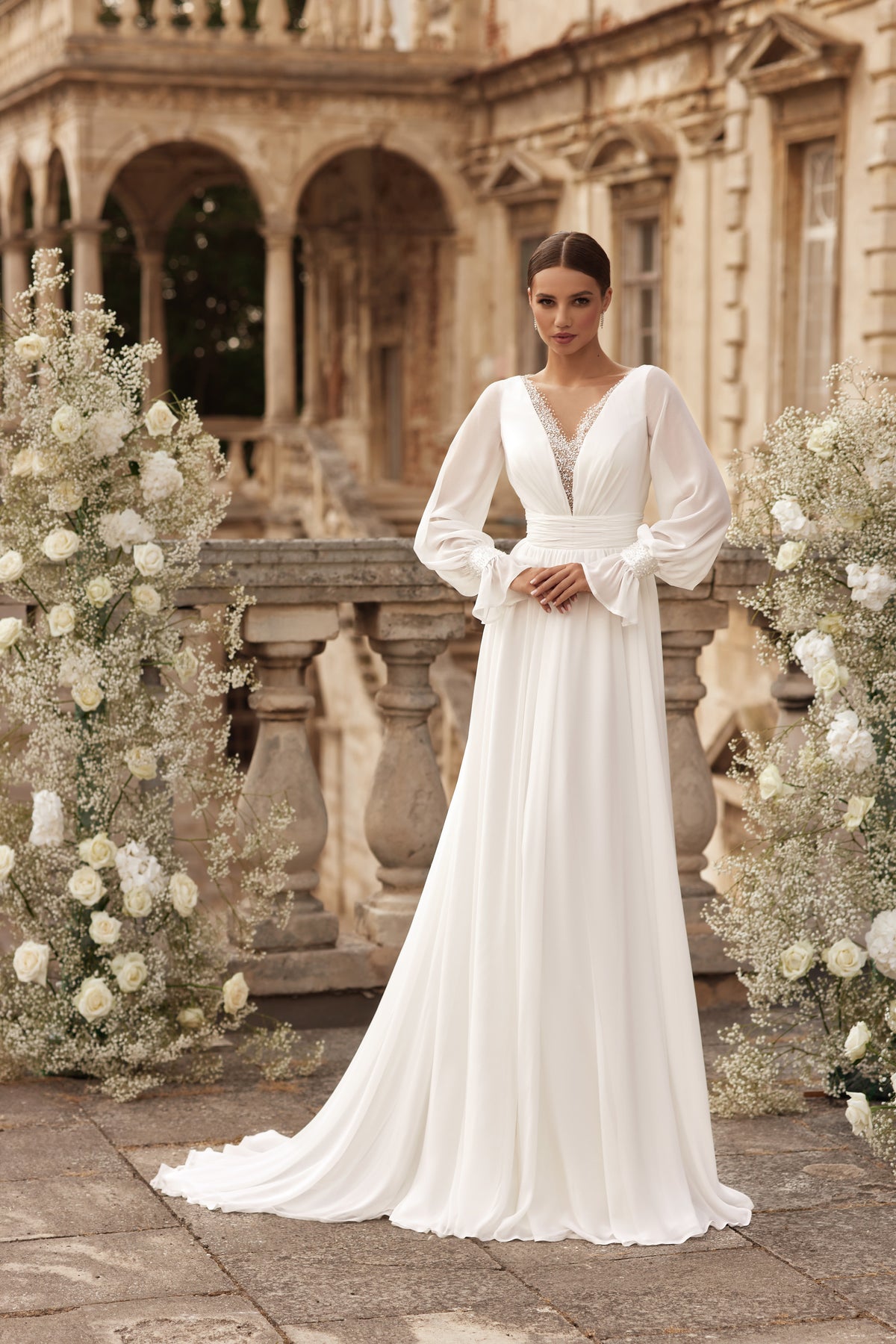 Ivory A-line wedding dress with a beaded V-neckline, sheer bishop sleeves, and a flowing train