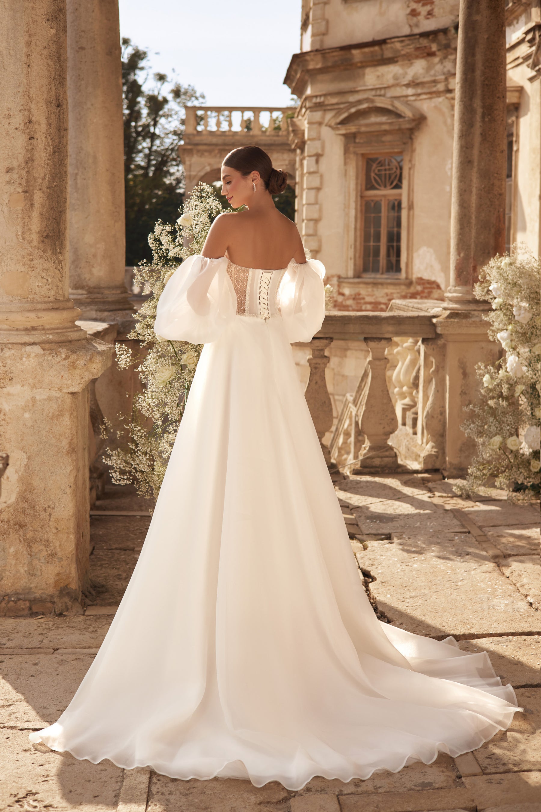 Ivory wedding dress with off-the-shoulder puff sleeves, an open corset-style back, and sweeping train