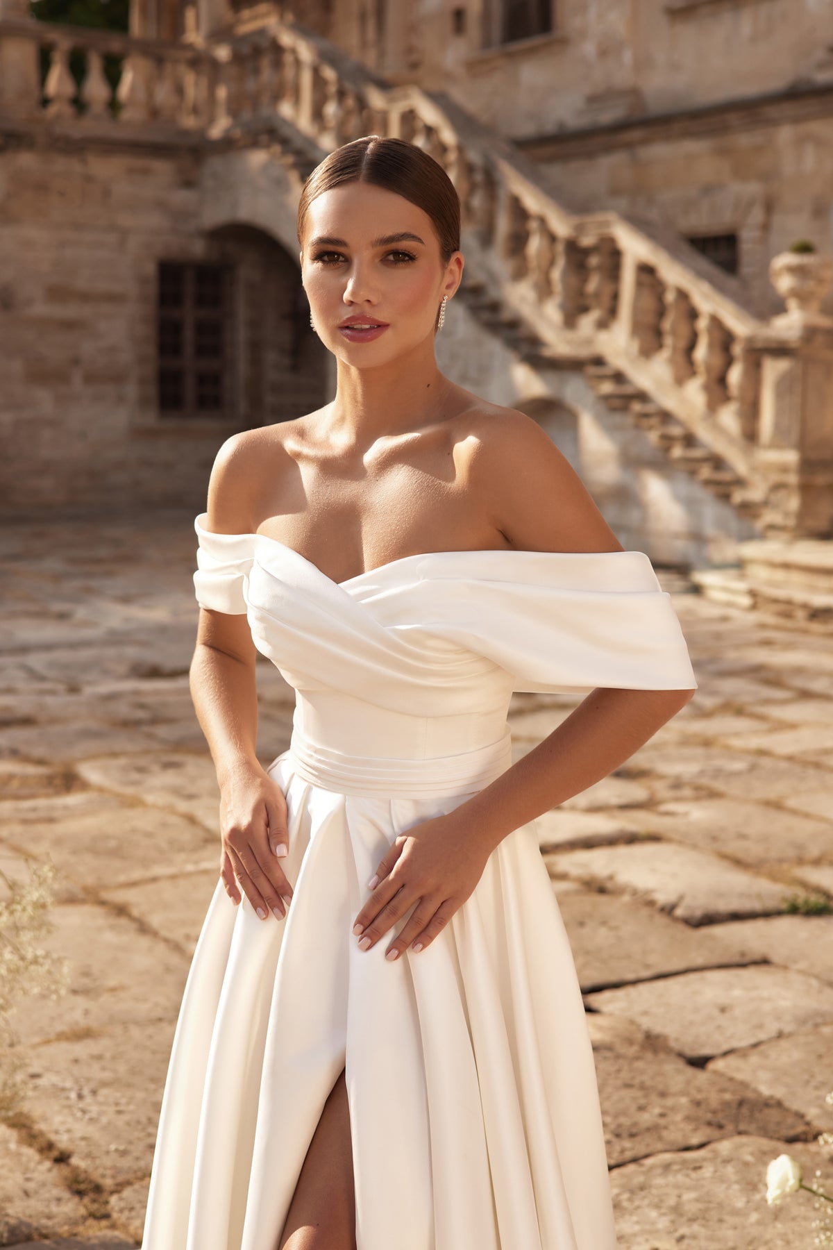 Ivory A-line wedding dress with an off-the-shoulder draped neckline, ruched bodice, and front slit