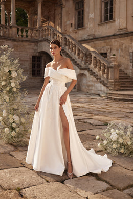 Ivory A-line wedding dress with an off-the-shoulder neckline, high slit, and flowing train