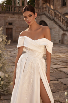 Close-up of an ivory wedding dress with a draped off-the-shoulder neckline, sparkling bodice, and thigh-high slit
