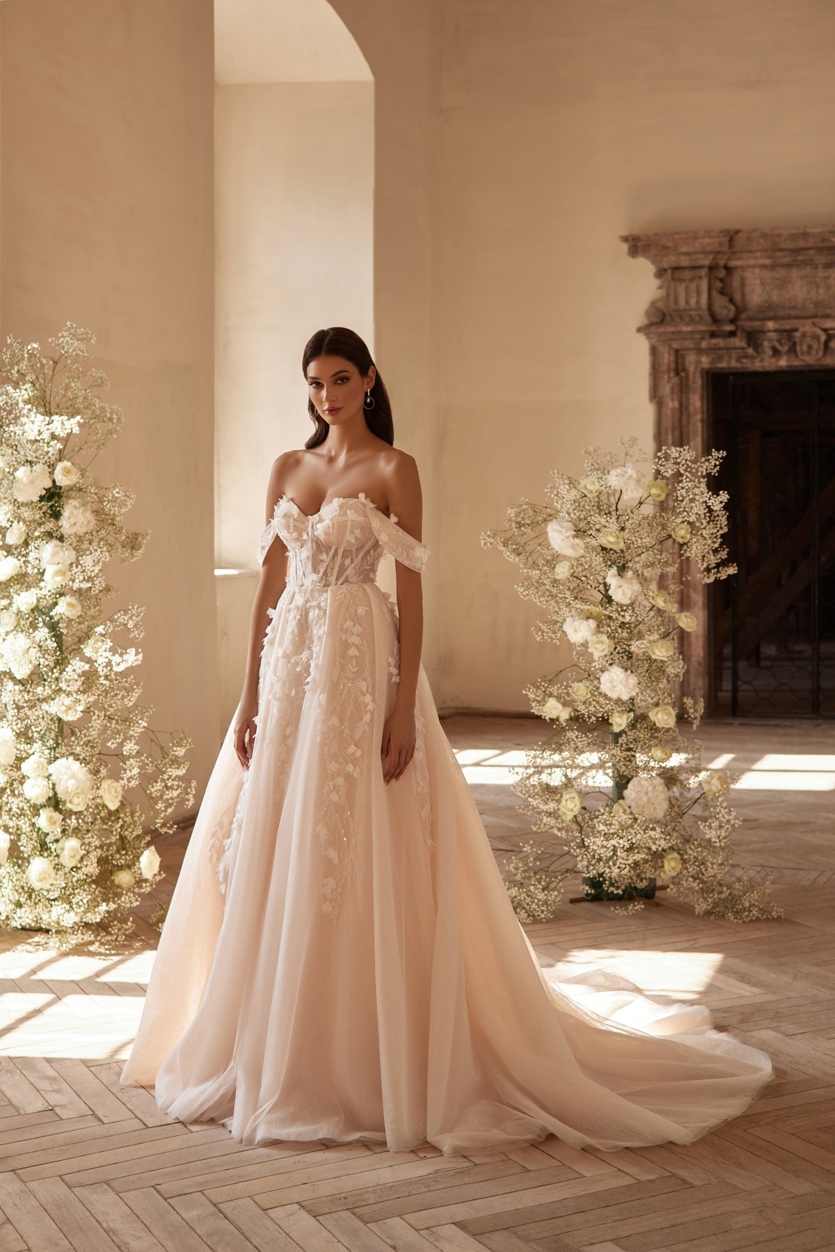 Ivory wedding dress with a corset bodice, off-the-shoulder sleeves, floral appliqués, and flowing train