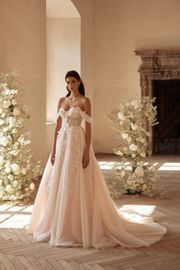 Ivory wedding dress with a corset bodice, off-the-shoulder sleeves, floral appliqués, and flowing train