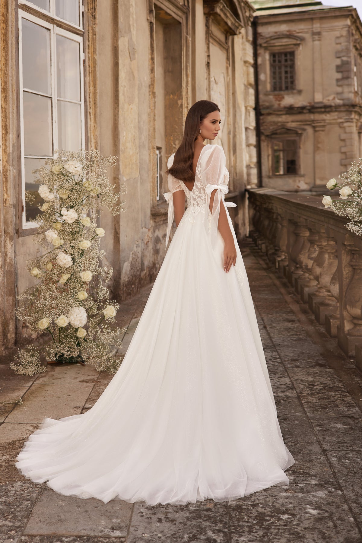 Back of an ivory wedding dress with a low open back, puff sleeves, waist ties, and a long train