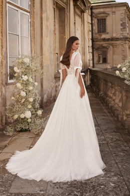 Back of an ivory wedding dress with a low open back, puff sleeves, waist ties, and a long train
