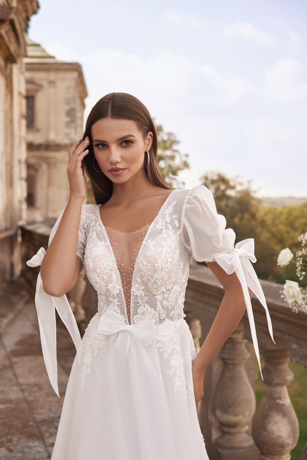 Close-up of an ivory wedding dress with floral lace, a sheer V-neck panel, and puff sleeves with ribbon ties