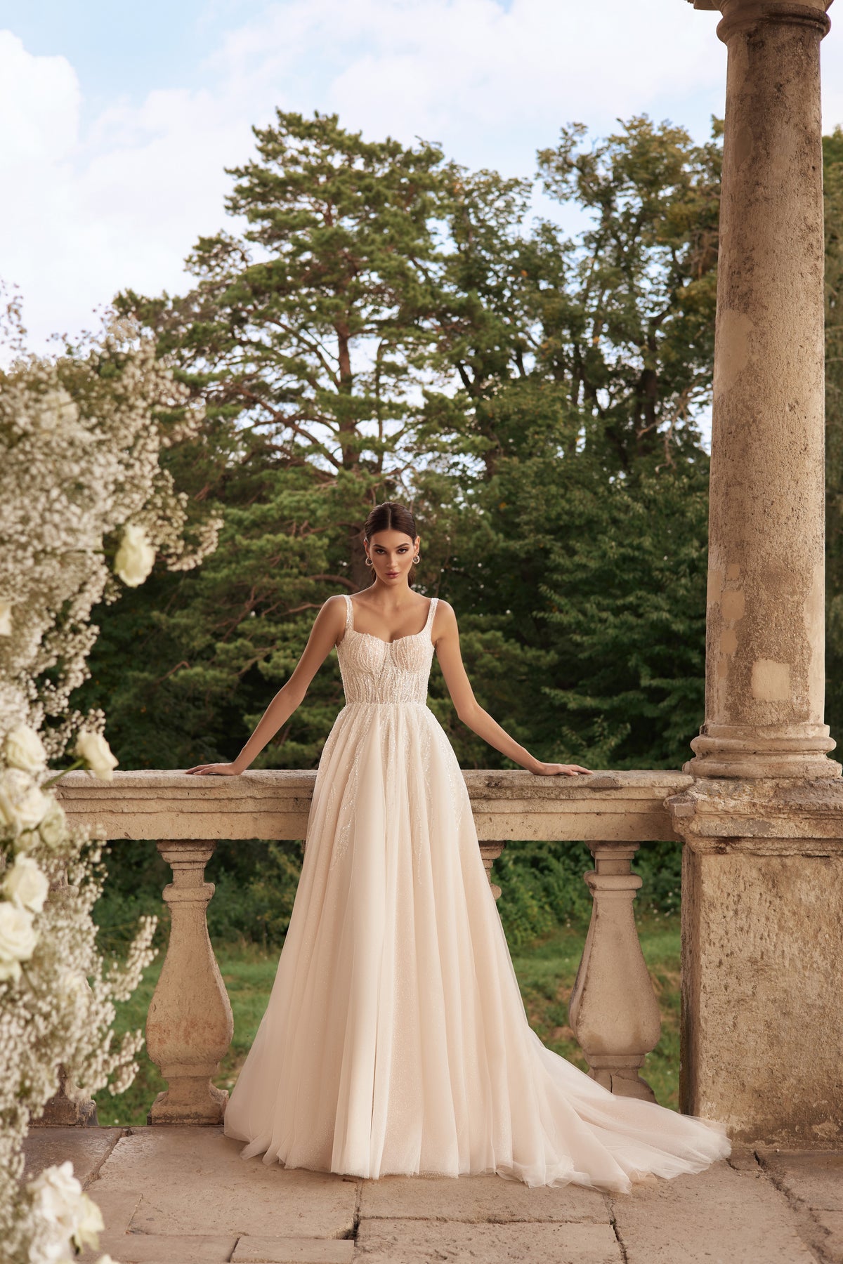 Ivory A-line wedding dress with a beaded bodice, slim straps, flowing skirt, and sweeping train