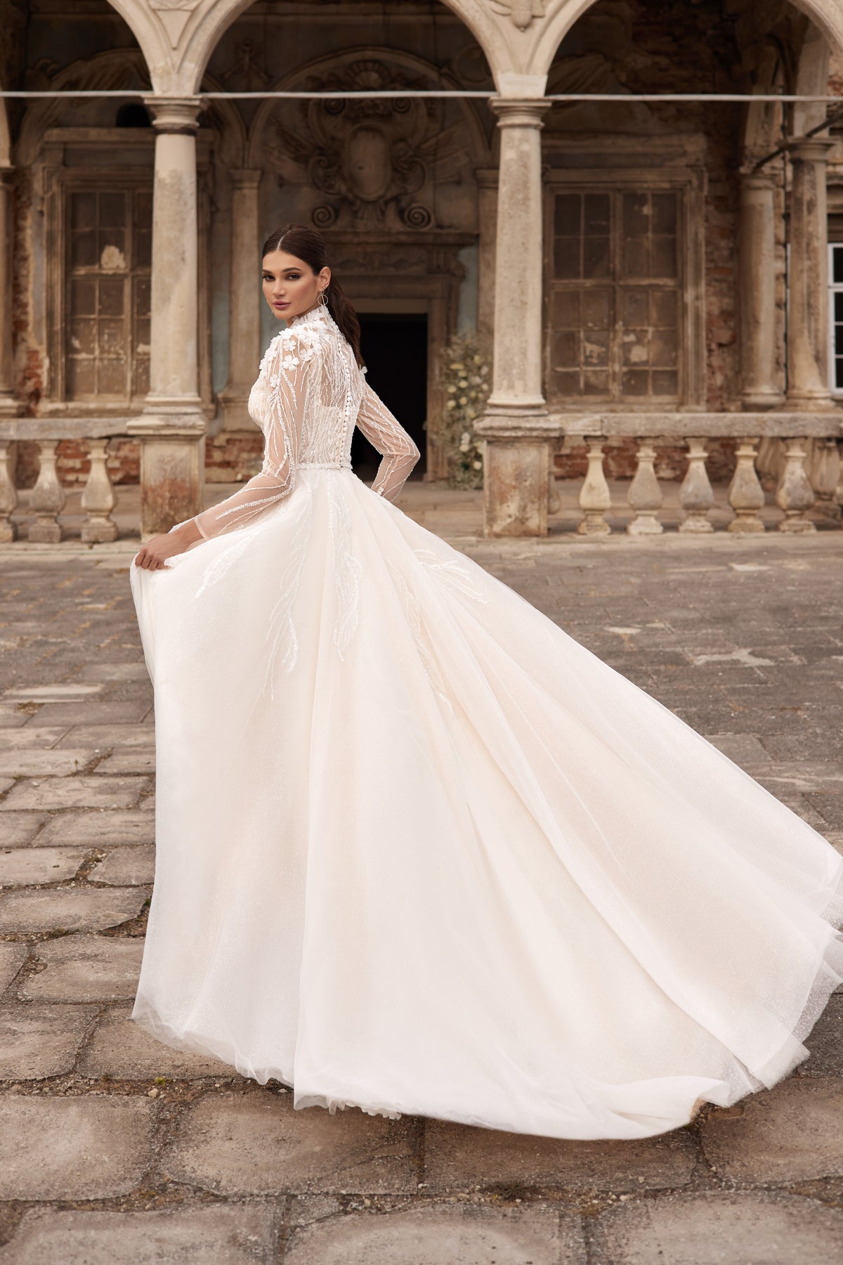 Three-quarter back view of an ivory wedding dress with a sheer lace back, long sleeves, full skirt, and extended train