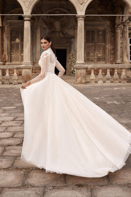 Three-quarter back view of an ivory wedding dress with a sheer lace back, long sleeves, full skirt, and extended train