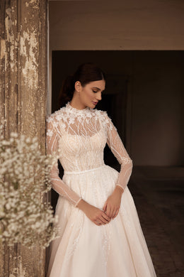 Close-up of an ivory wedding dress with a high illusion neckline, sheer lace sleeves, and sparkling embellished bodice