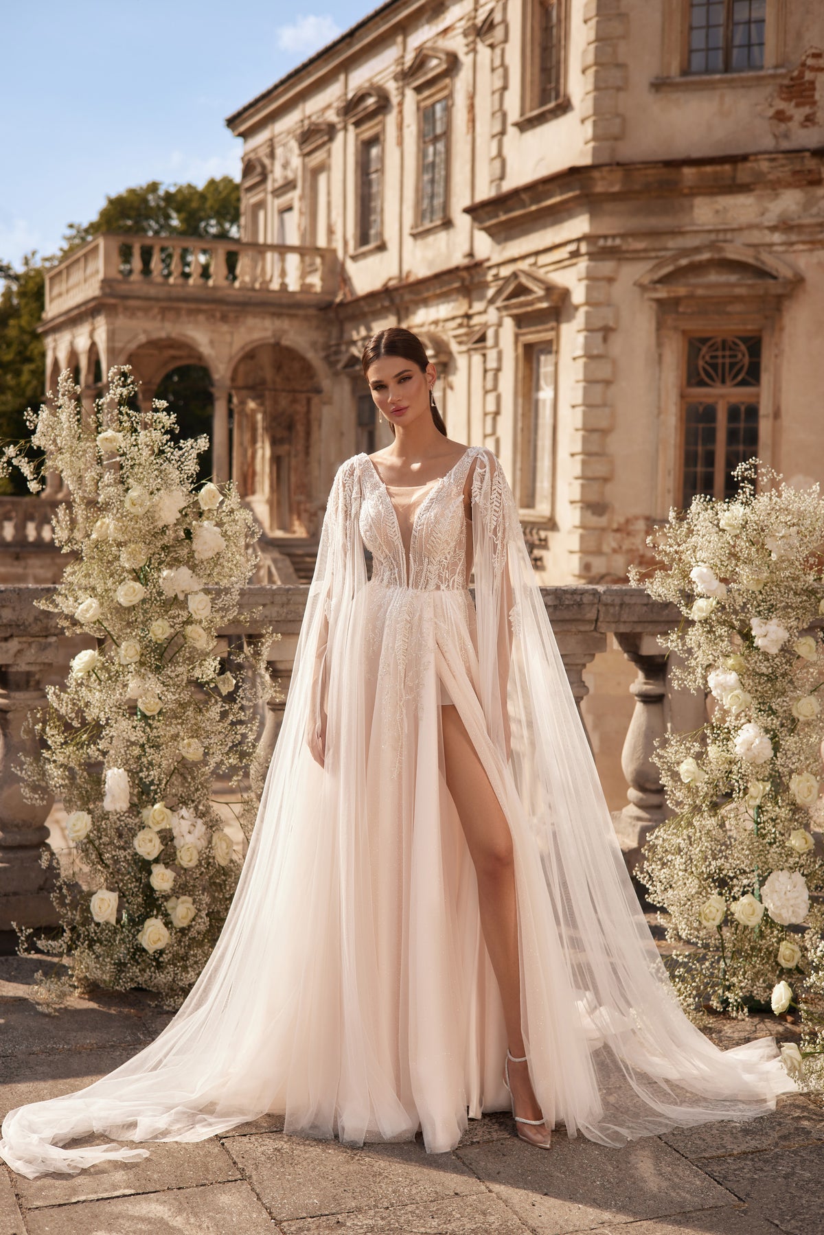 Ivory wedding dress with a sparkling sheer cape, embellished bodice, high slit, and sweeping train