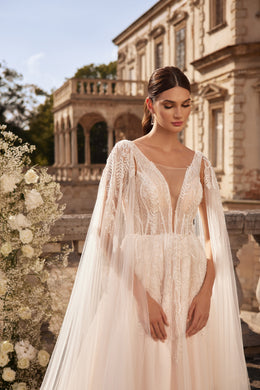 Close-up of an ivory wedding dress with a sheer beaded bodice, illusion neckline, and flowing cape