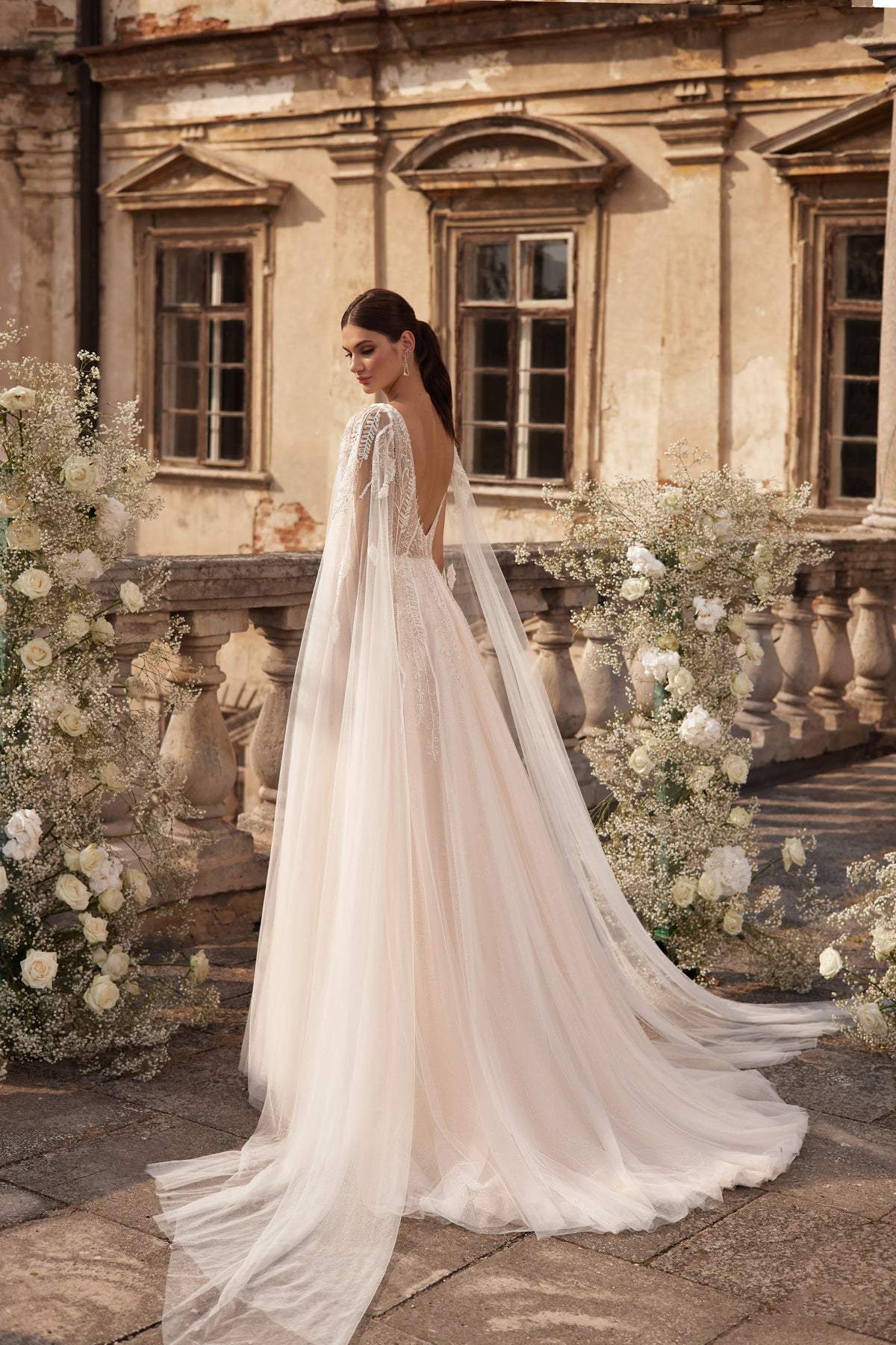 Back view of an ivory wedding dress showing a deep V back beneath a long sheer cape and trailing train