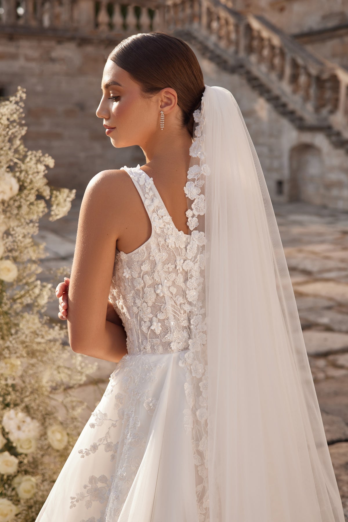 V-back wedding dress with floral lace detailing, narrow straps, and a long sheer veil-like train