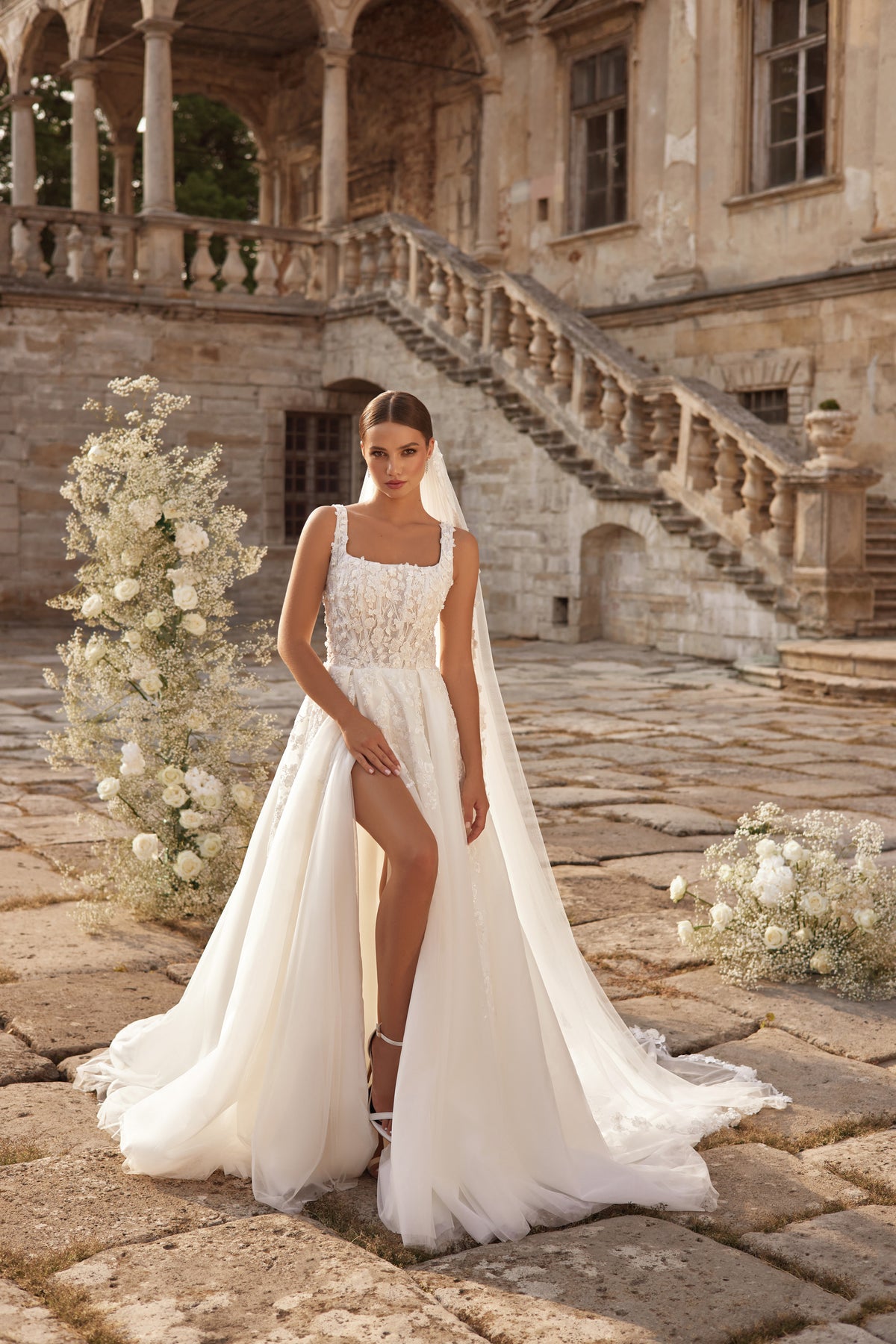 Ivory wedding dress with a square neckline, lace bodice, high thigh slit, and sweeping train