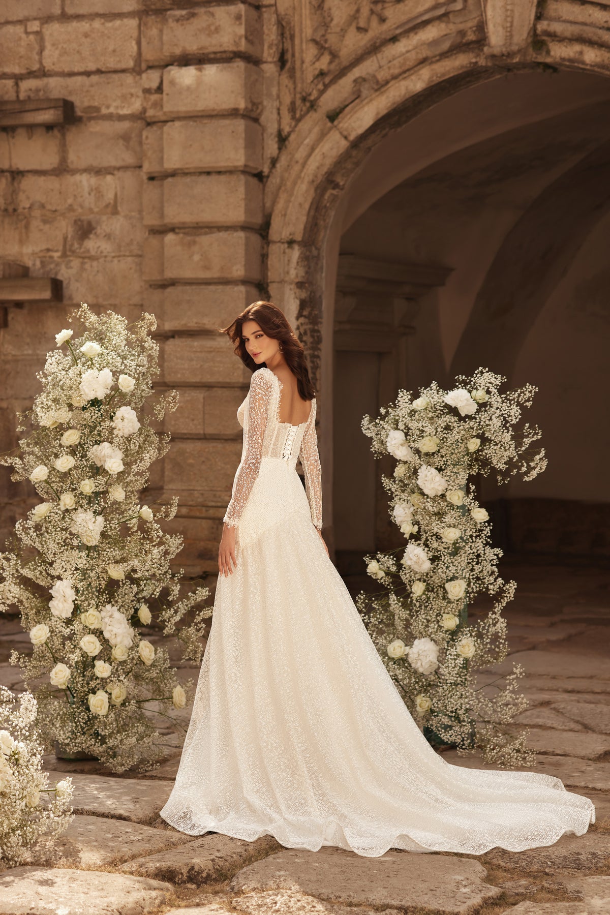 Ivory wedding dress with a low open back, long lace sleeves, fitted silhouette, and flowing train