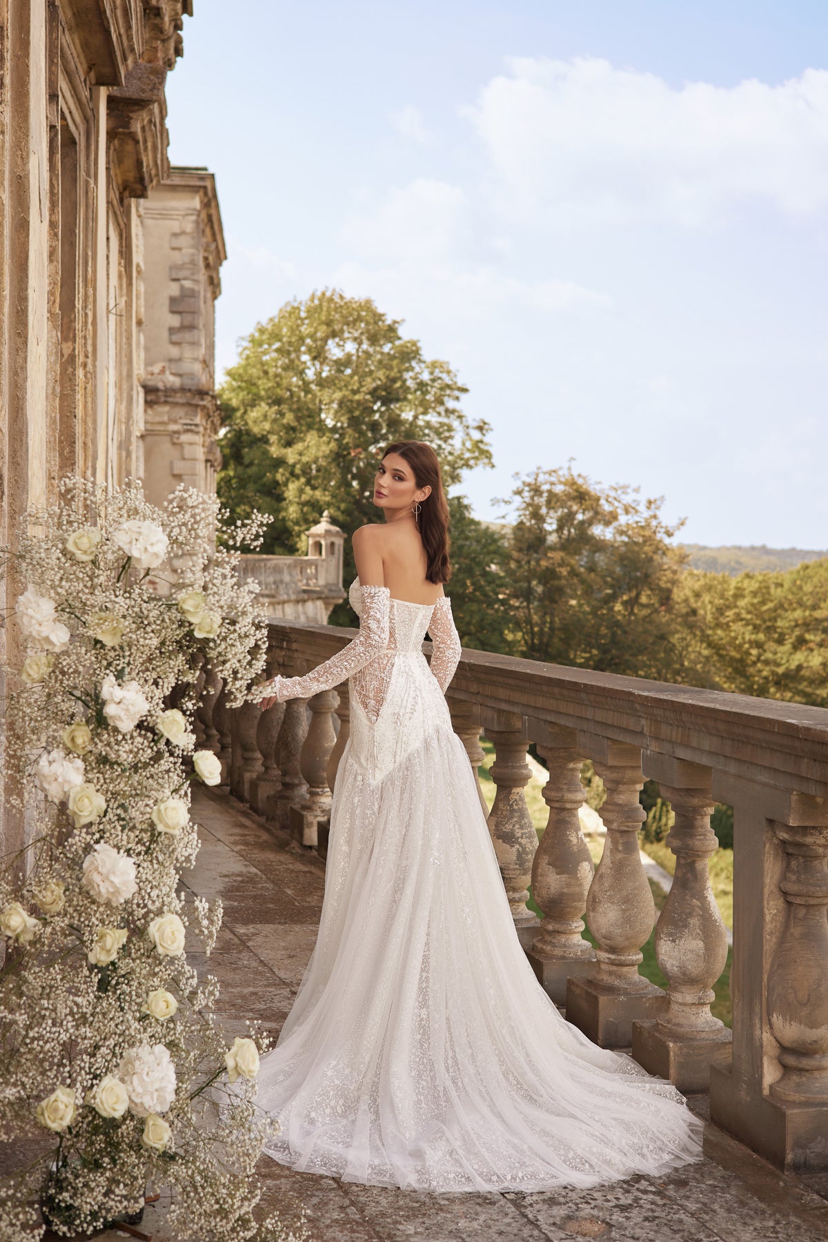 Open-back ivory wedding dress with off-the-shoulder lace sleeves, fitted skirt, and a long flowing train