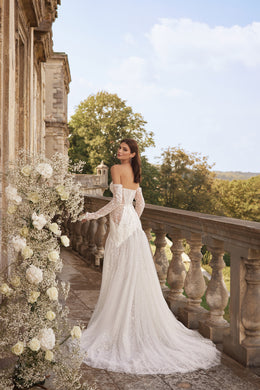 Open-back ivory wedding dress with off-the-shoulder lace sleeves, fitted skirt, and a long flowing train
