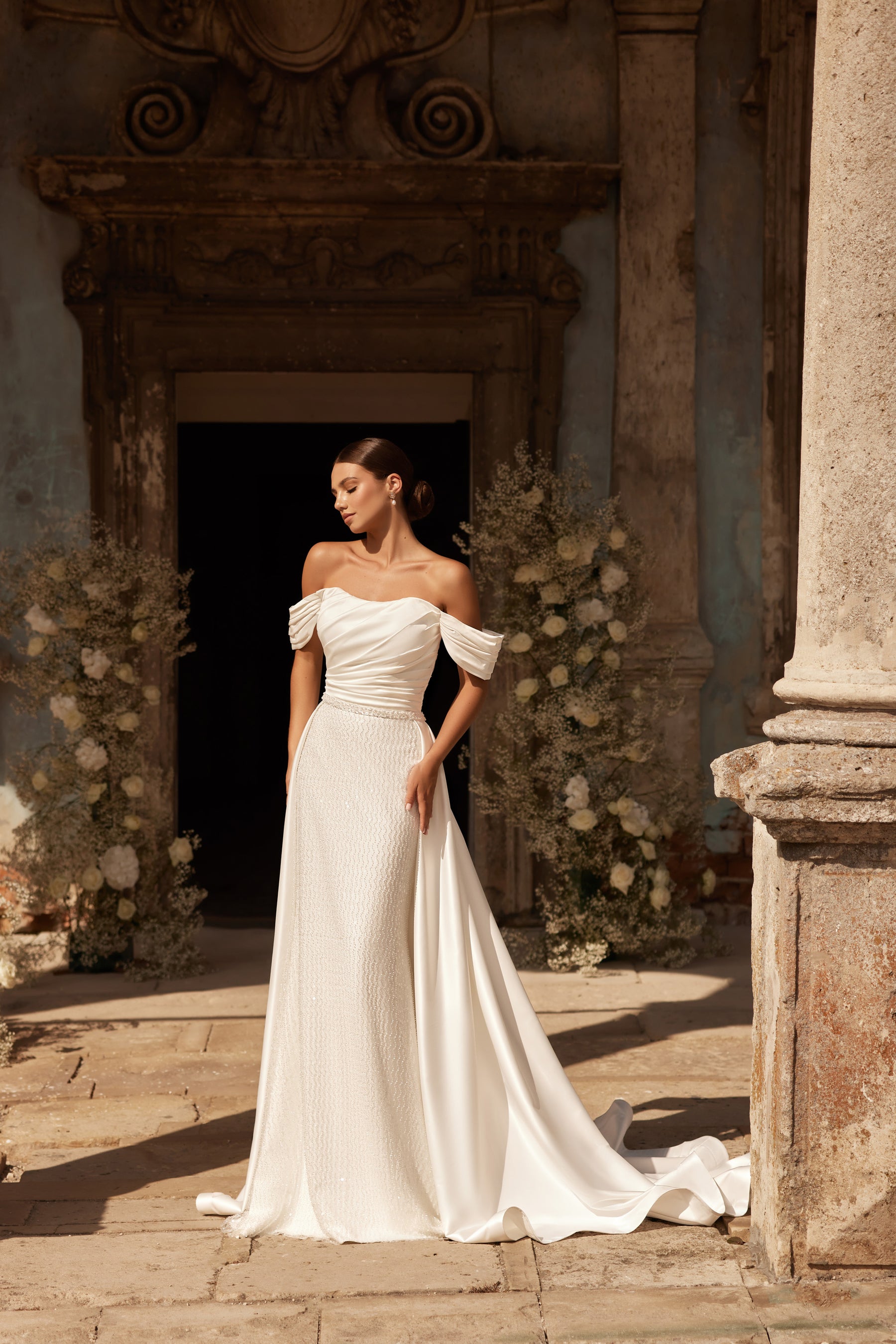Ivory wedding dress with a fitted beaded skirt, off-the-shoulder sleeves, and a flowing overskirt
